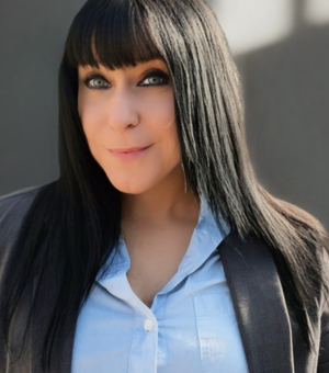 Portrait of student Blackmer, wearing a light blue button-up shirt and a dark blazer, smiling at the camera against blurred background